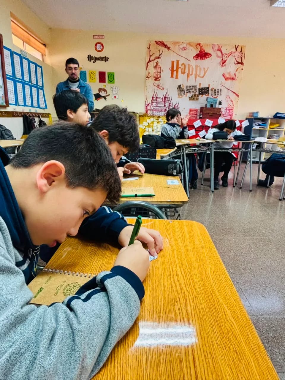 Estudiantes escriben en sus pupitres en una sala decorada para una jornada literaria.