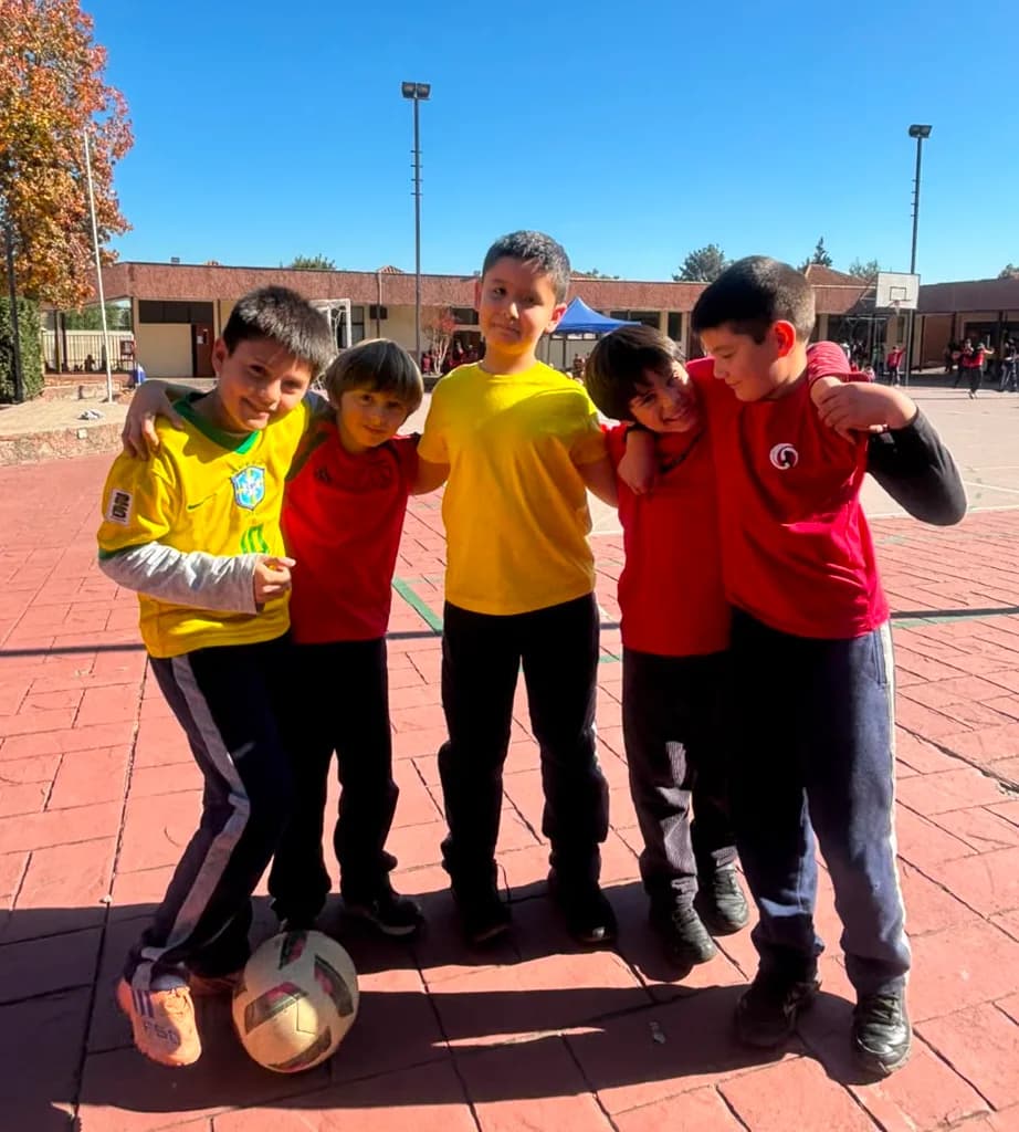 Cinco estudiantes se abrazan en el patio del colegio después de un partido, con un balón a los pies.