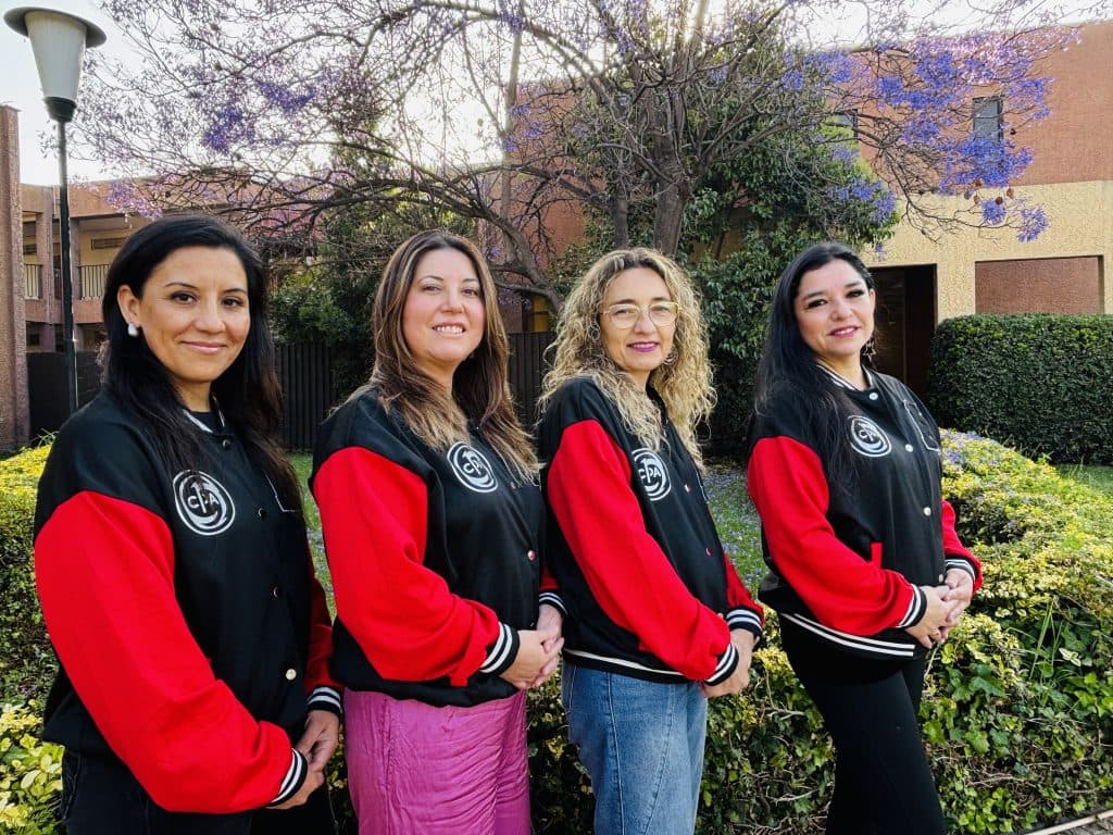 Cuatro integrantes del Centro de Padres posan en el jardín del colegio con la chaqueta del CEPA.