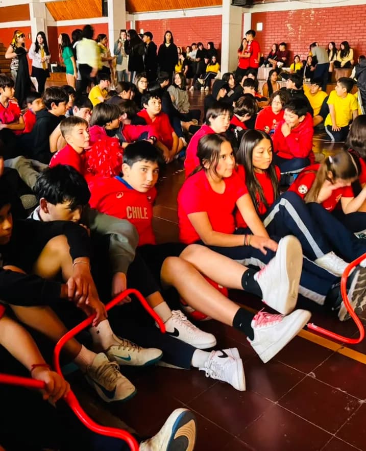 Estudiantes sentados en el piso del gimnasio con vallas naranjas, durante una jornada deportiva.