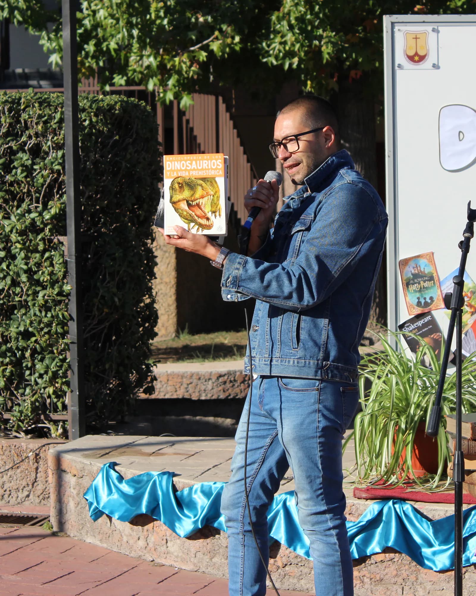 Un integrante de la comunidad presenta un libro junto a la gráfica del Día del Libro.
