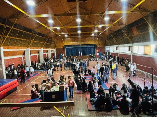 Vista amplia del gimnasio durante una jornada de convivencia: colchonetas de gimnasia en el suelo, grupos de estudiantes sentados y otros de pie contra los muros.