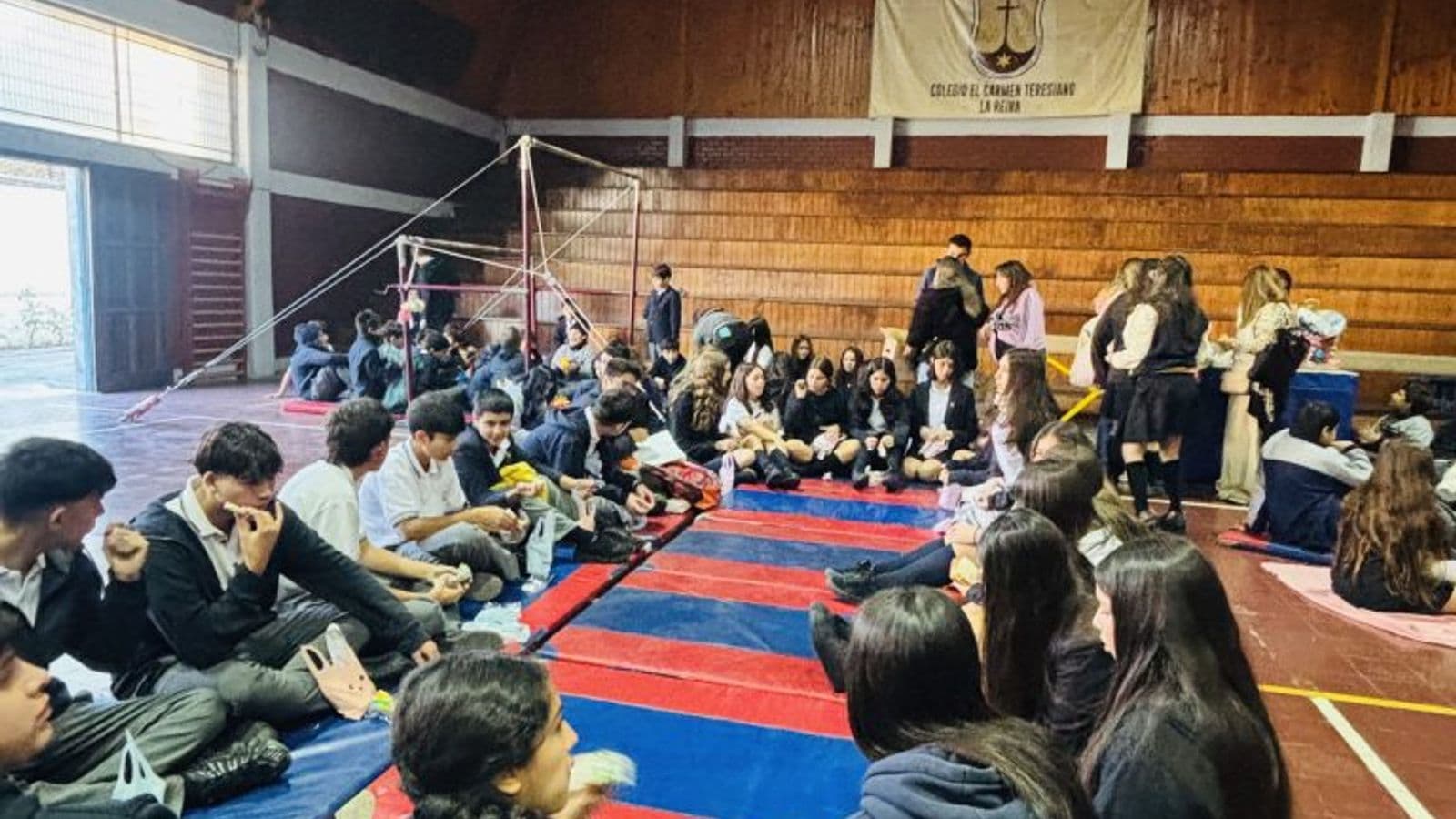 Jornada de convivencia en el gimnasio: estudiantes sentados en grupos sobre colchonetas rojas y azules compartiendo una colación.