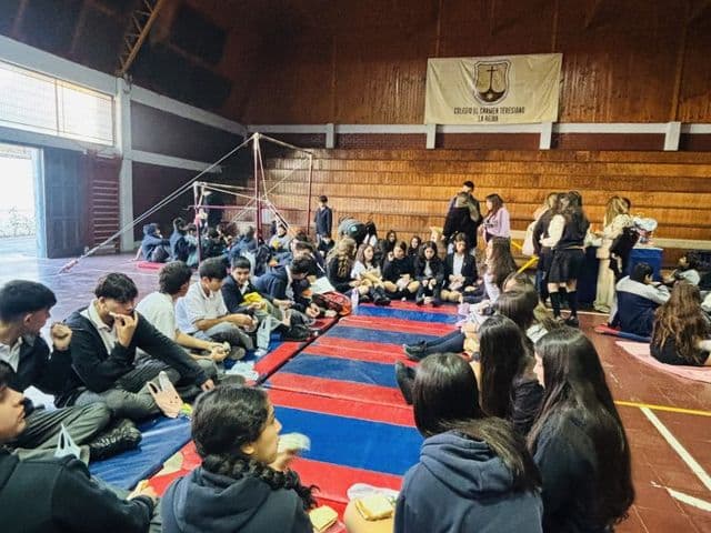 Jornada de convivencia en el gimnasio: estudiantes sentados en grupos sobre colchonetas rojas y azules compartiendo una colación.