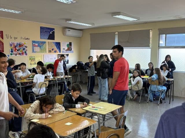 Sala de clases con los pupitres agrupados en islas para trabajo en equipo, murales de trabajos en la pared y estudiantes escribiendo.