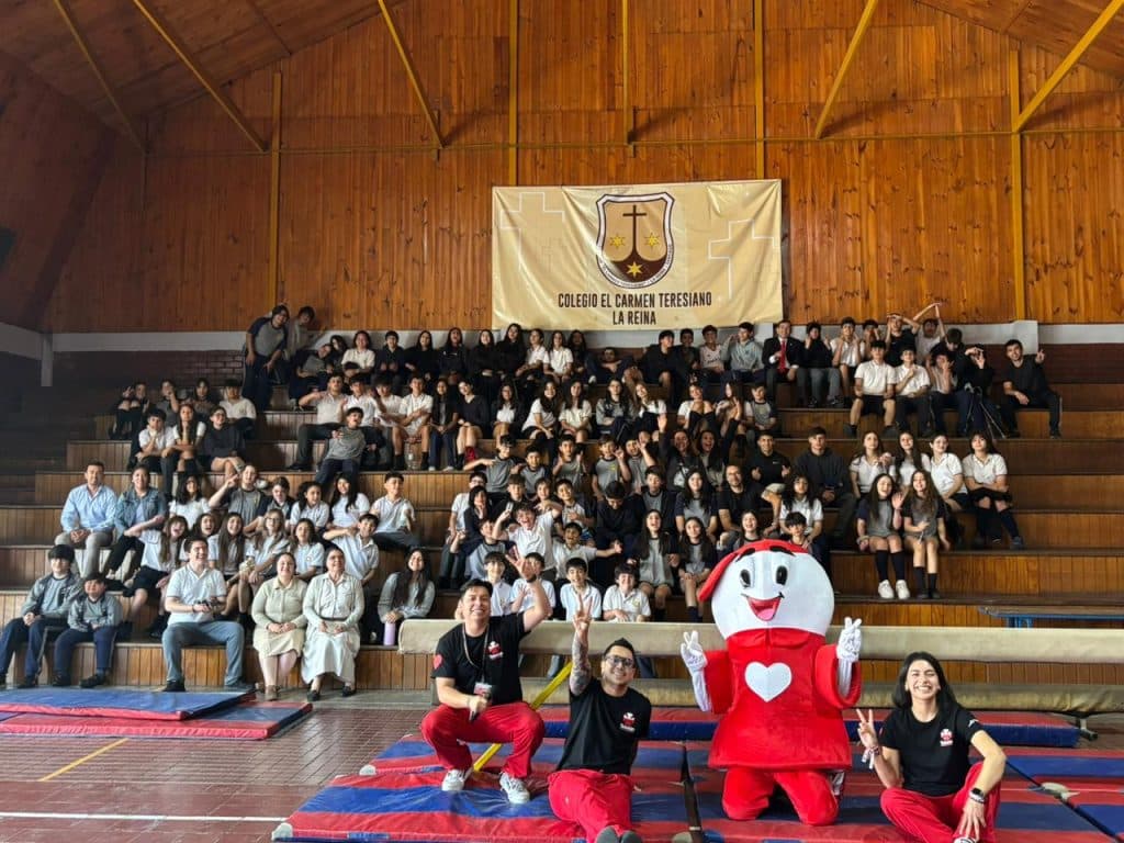Fotografía de toda la comunidad escolar en las graderías del gimnasio, bajo un lienzo con el escudo y el nombre del Colegio El Carmen Teresiano La Reina.