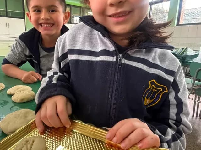 Dos estudiantes de ciclo menor muestran sonrientes sus panes recién horneados.